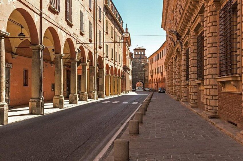Una strada fiancheggiata da edifici ad arco, cielo sereno e una torre in lontananza. 1