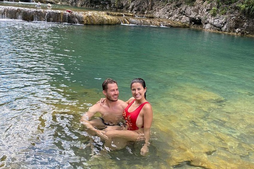 Two people sitting in a clear water body with a rocky background. 4