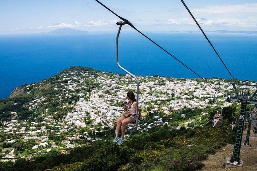 A person on a cable car over a coastal landscape with houses below. 1