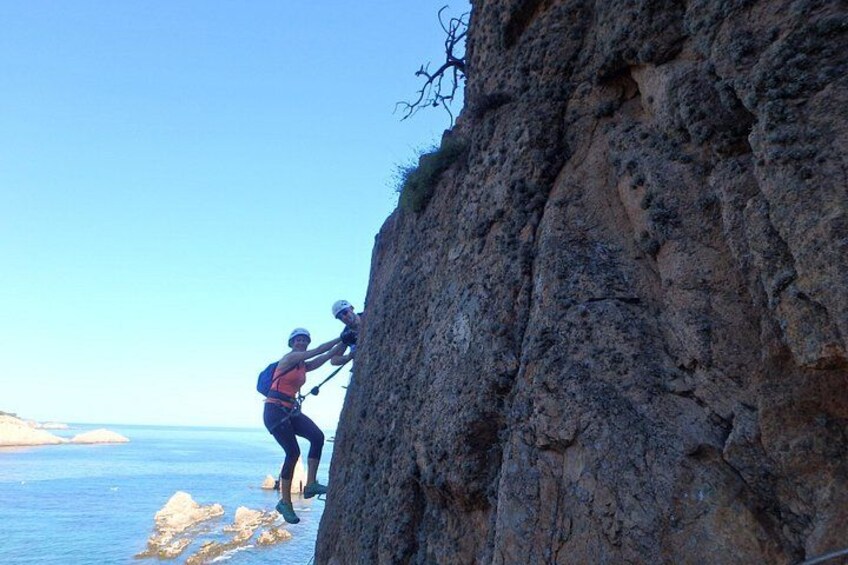 A person climbing a steep rocky cliff by the sea. 3