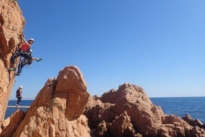 A person rock climbing on a cliff with a clear blue sky and ocean in the background. 1