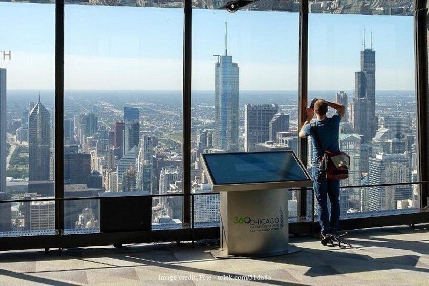 Una persona de pie junto a una ventana con vista a la ciudad, un atril con el texto '360CHICAGO' y un cielo despejado. 3