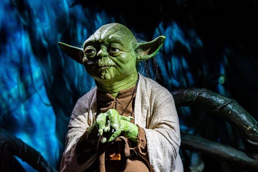 A character with green skin and pointed ears, dressed in a robe, sitting with hands clasped. 3