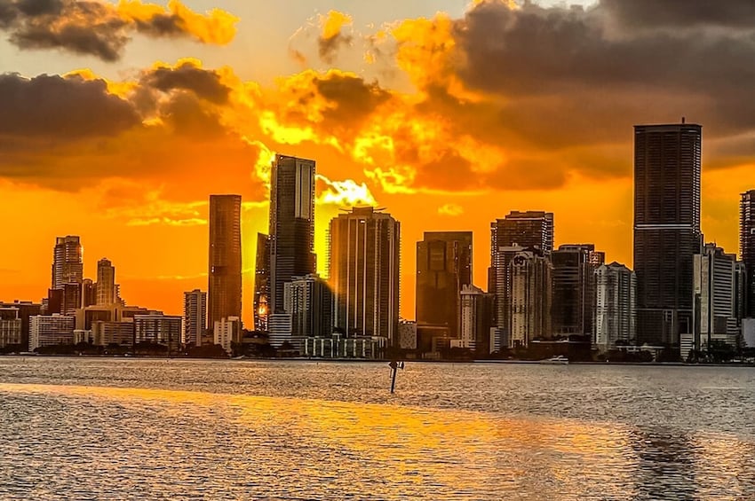A city skyline at sunset with tall buildings silhouetted against a vibrant orange sky. 1