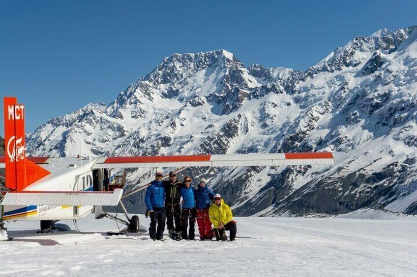 A group of people posing in front of a small aircraft on a snowy mountain. 2