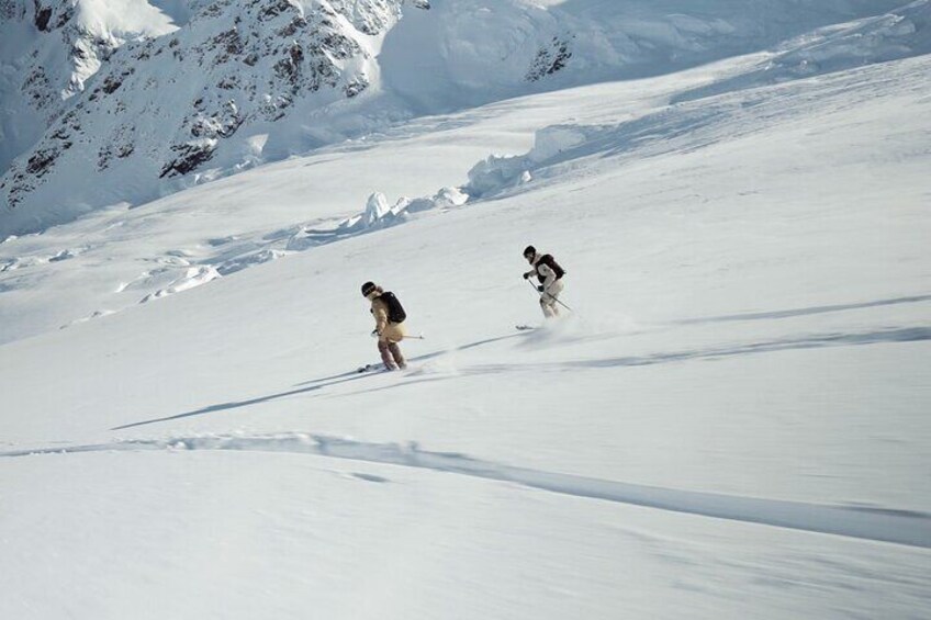 Two skiers descending a snow-covered slope with a mountainous backdrop. 1
