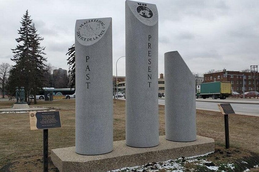 Three stone monuments with inscriptions, a statue, and a bus in the background. 5