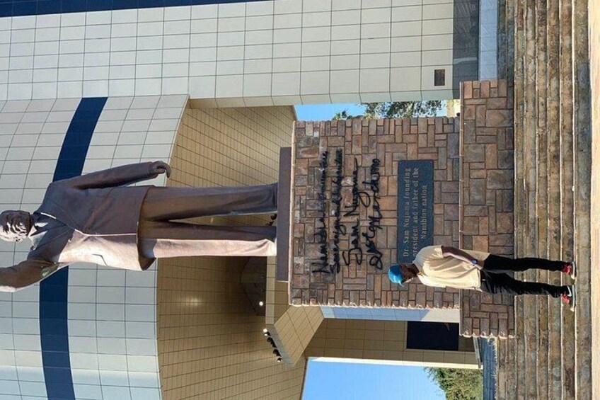 A statue of a man in a suit, a plaque with text, and a person standing in front of the statue. 5