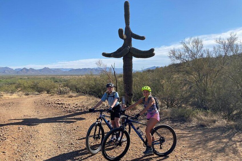 Two cyclists on a dirt road with a large saguaro cactus in the background. 3