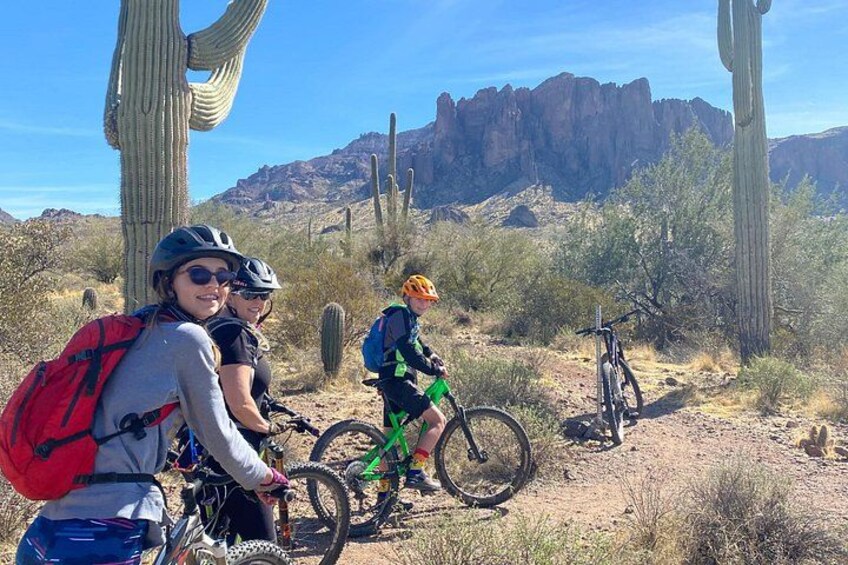 Three people on mountain bikes in a desert landscape with cacti and rocky terrain. 4