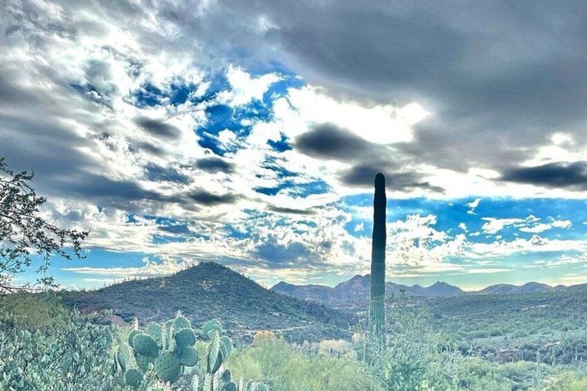 A tall, narrow tower amidst a desert landscape with mountains in the background and a partly cloudy sky. 2