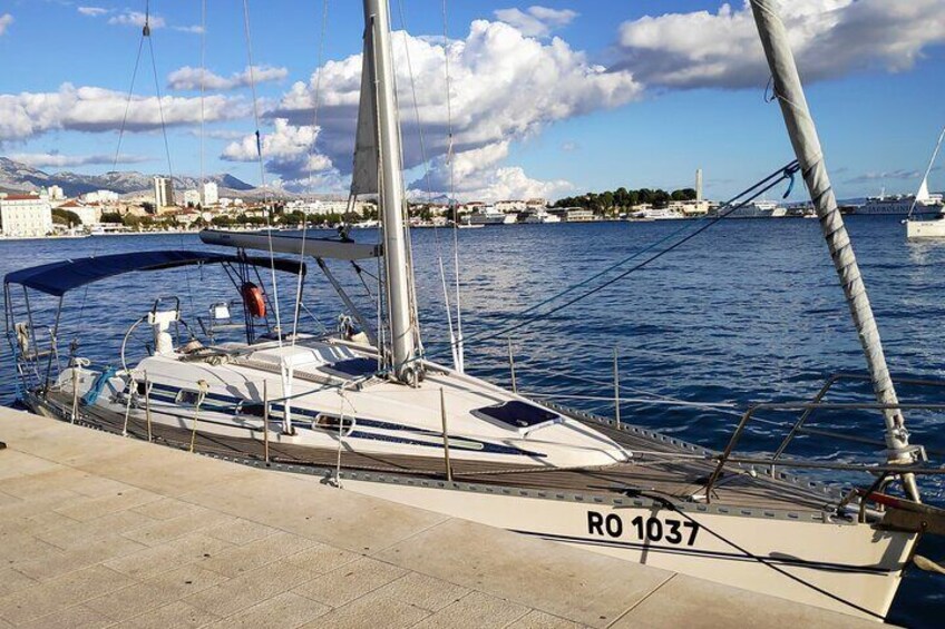 A sailboat docked at a marina with a clear sky and distant cityscape. 2