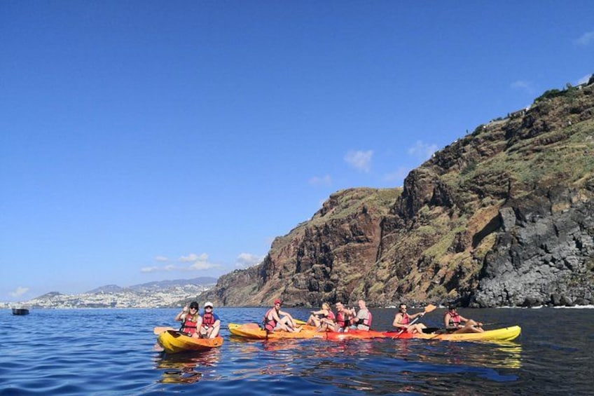 A group of people kayaking on calm water with a rocky coastline in the background. 3