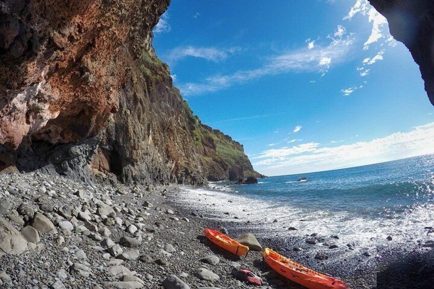 A rocky beach with kayaks, a cliff, and the ocean. 2