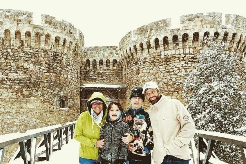 A group of people standing in front of a stone castle with arched windows and a snow-covered tree. 4