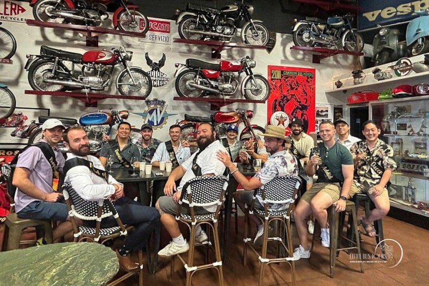 A group of people seated in a motorcycle shop with various motorcycles displayed on the walls. 3