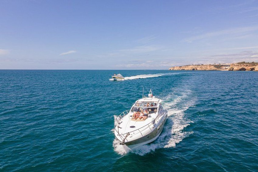 A white boat with passengers on a calm sea, another boat in the distance, and a rocky coastline. 1