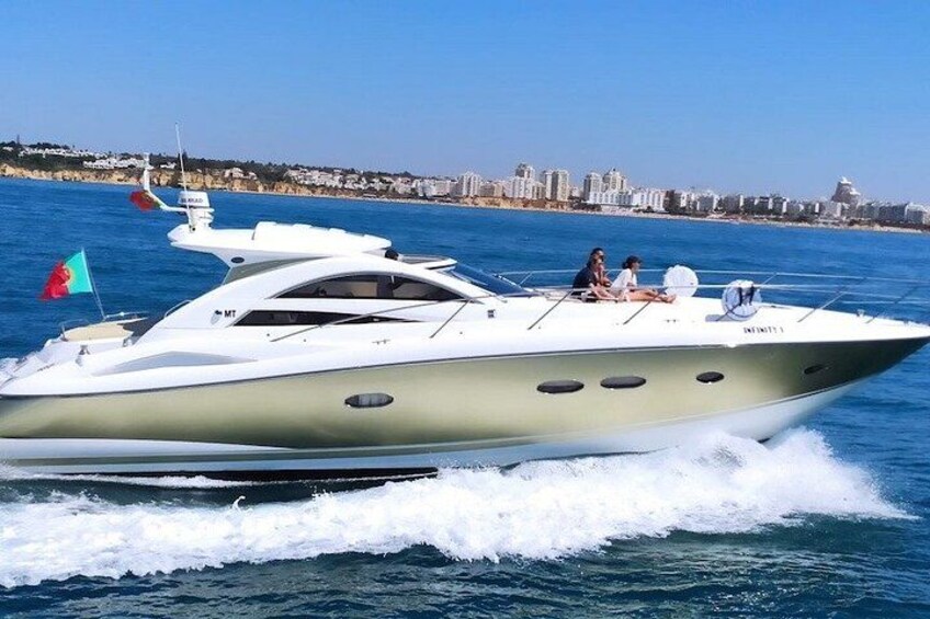 A white yacht with a green stripe, two flags, and a cityscape in the background. 2