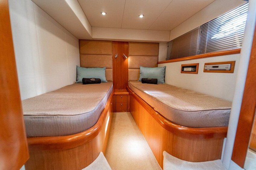 A narrow cabin with two wooden bunk beds, a small window with blinds, and a wooden headboard. 4