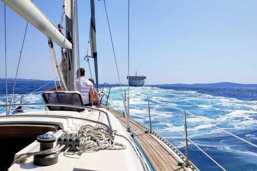 A sailboat on the sea with two people on deck, ropes, and a steering wheel. 1