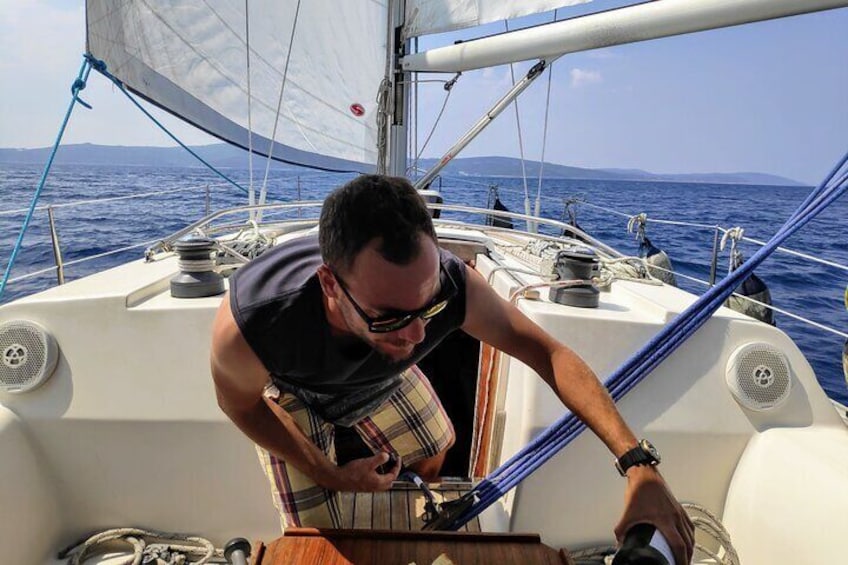 A man on a sailboat, leaning over the deck, looking at a device in his hands. 2