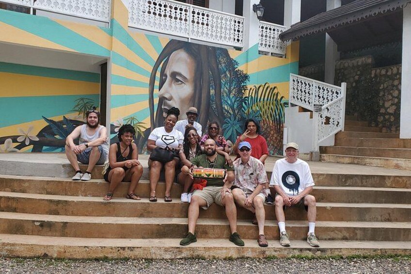 A group of people sitting on steps in front of a building with a mural. 5