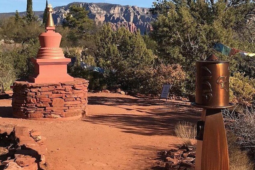 A red Buddhist stupa, a copper water spout, and a sign in a desert landscape with mountains in the background. 2