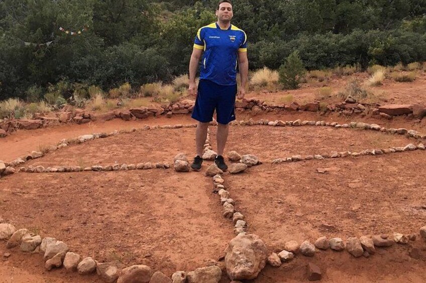 A person standing in a circular stone arrangement in a dry, rocky landscape with sparse vegetation. 5