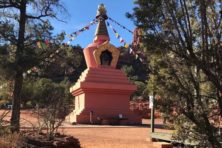 A red stupa with a golden spire, surrounded by trees and flags. 4