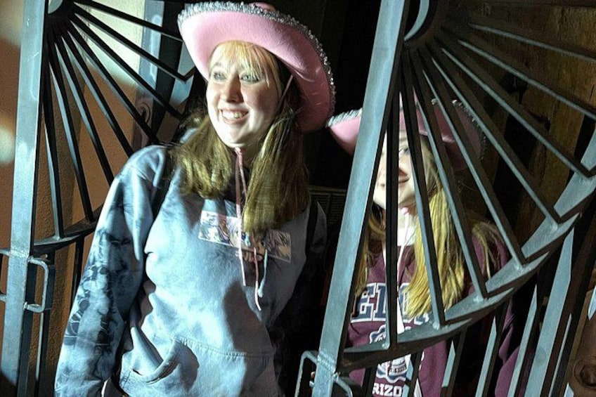 A person wearing a pink hat and a blue jacket standing in front of a metal gate. 4