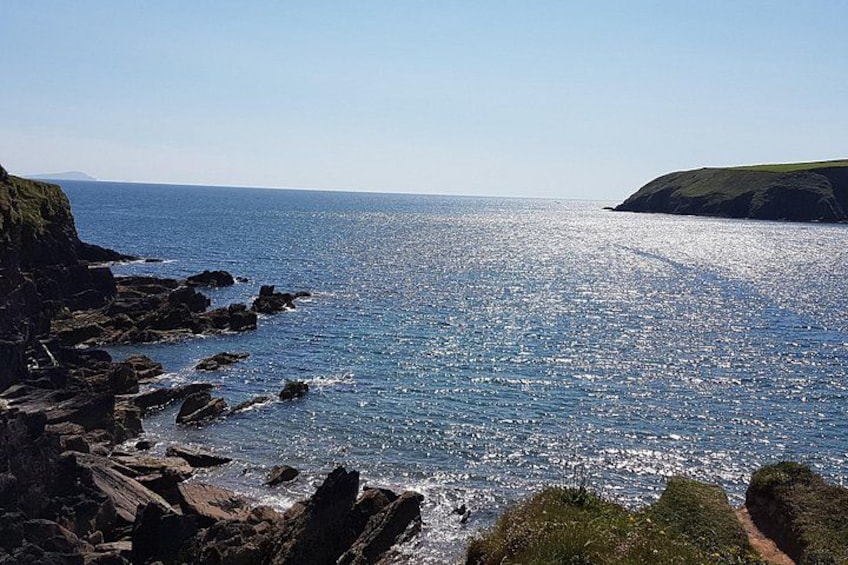 Eine Küstenlandschaft mit felsigen Klippen, tiefblauem Meer und einer entfernten Landmasse. 2