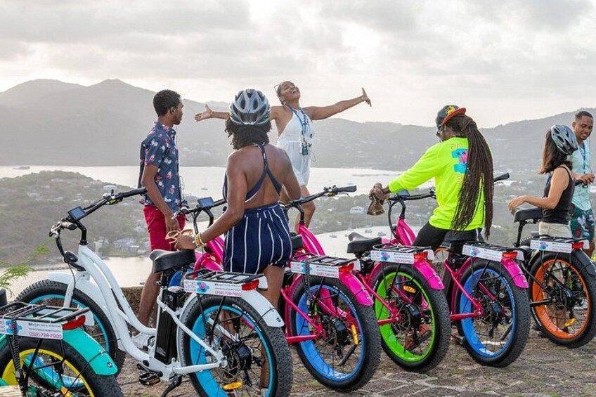 A group of people on electric bikes by a lakeside with mountains in the background. 1