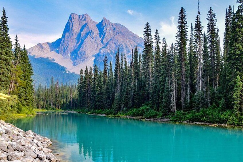 A turquoise lake surrounded by dense coniferous forest and a prominent mountain range. 2