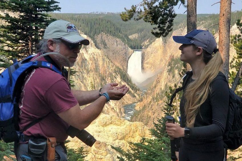 Two people standing near a waterfall with a mountainous landscape in the background. 2