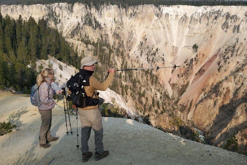Two people hiking on a mountain trail with a rocky cliff in the background. 4