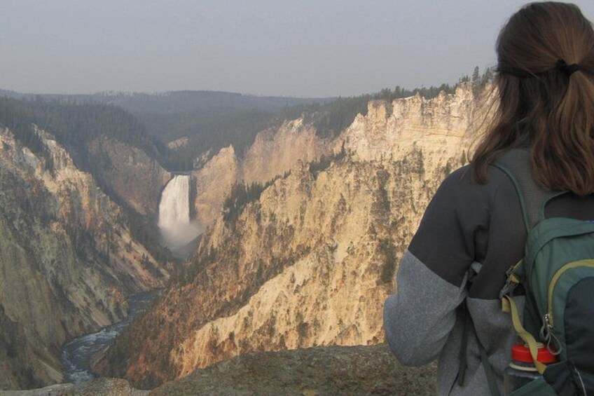 A person with a backpack overlooking a canyon with a waterfall. 3