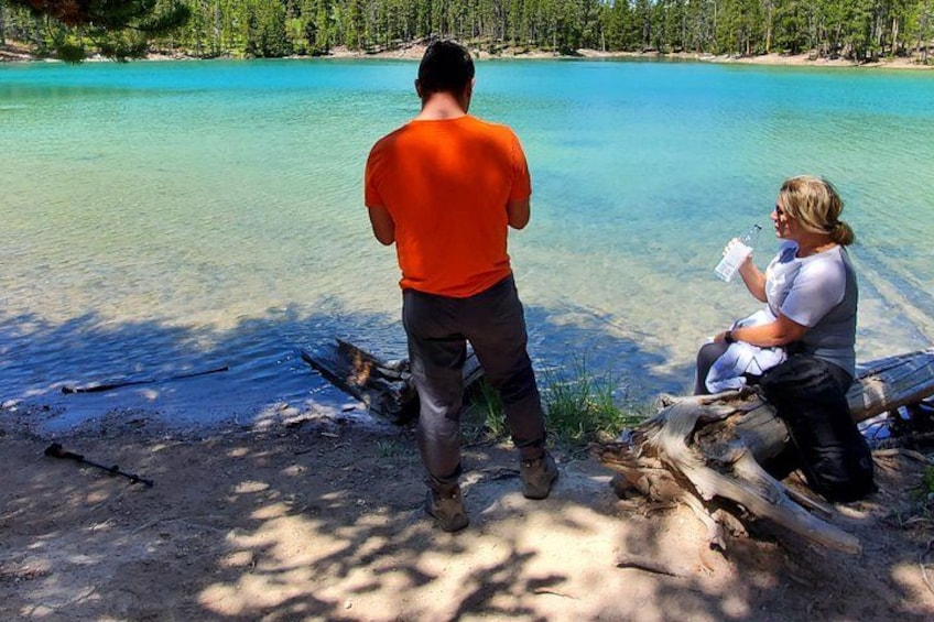 Two people by a clear lake with a forested shoreline. 4