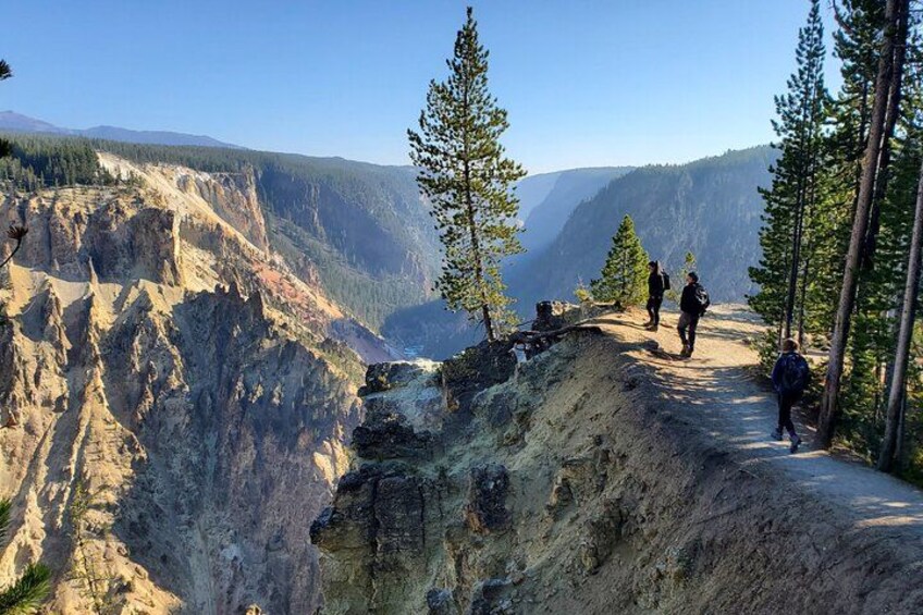 A canyon with hikers on a trail, surrounded by rocky cliffs and sparse trees. 1