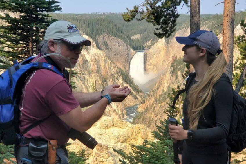 Two people standing near a waterfall with a mountainous landscape in the background. 3