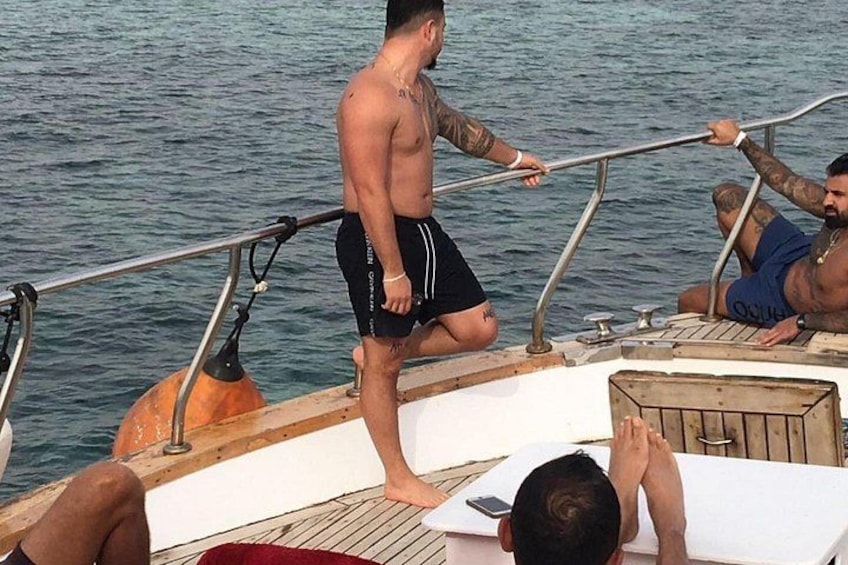 Un bote con gente en la cubierta, una de pie y dos sentadas, con agua al fondo. 3