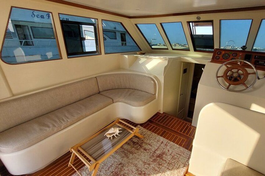A boat interior with a cushioned seating area, a steering wheel, and windows. 2