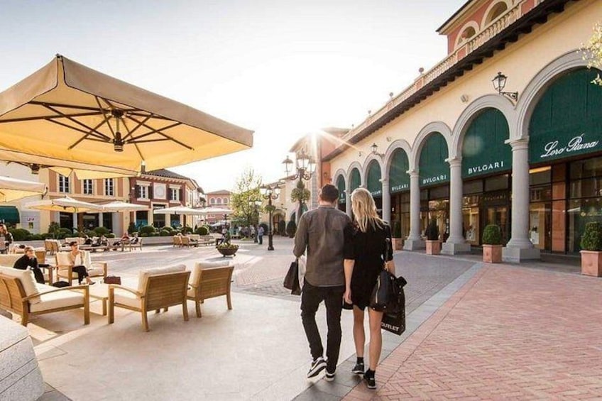 Una coppia passeggia in una zona commerciale con tavoli all'aperto e vetrine. 1