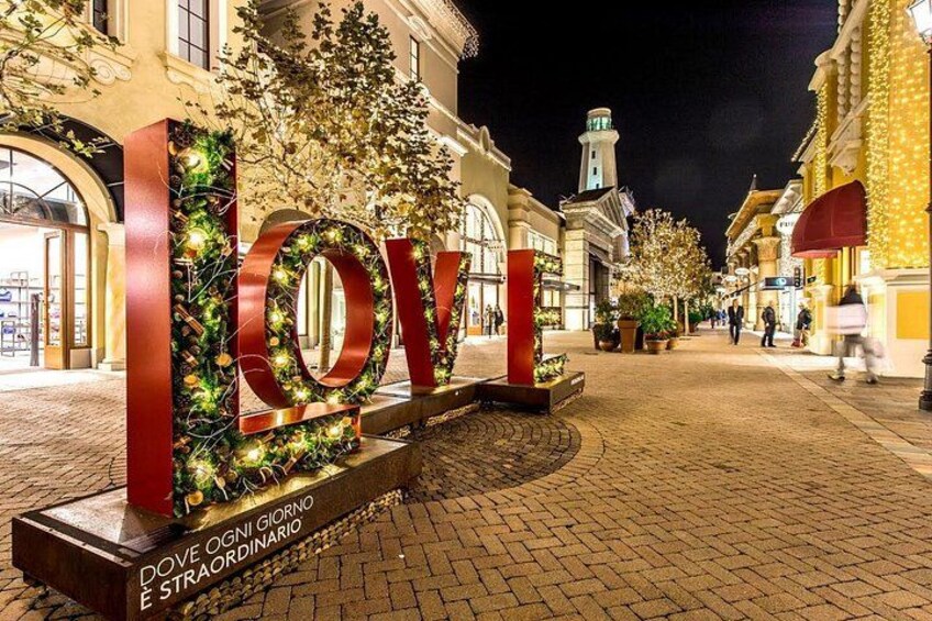 Un grande cartello luminoso con la scritta 'LOVE' e un'elaborata ghirlanda, posto in una strada acciottolata di notte. 4