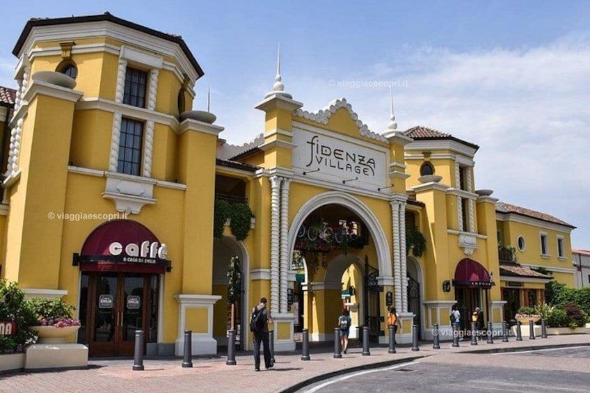 Un edificio giallo con un cartello che riporta 'FIDENZA VILLAGE' e un caffè chiamato 'caffè' con posti a sedere all'aperto. 5
