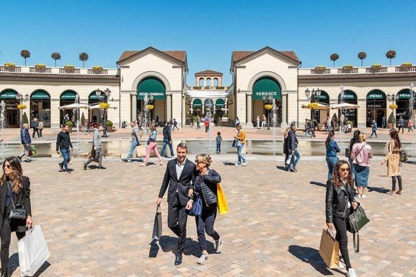 Una vivace piazza pubblica con persone che passeggiano, negozi e un cielo azzurro. 3