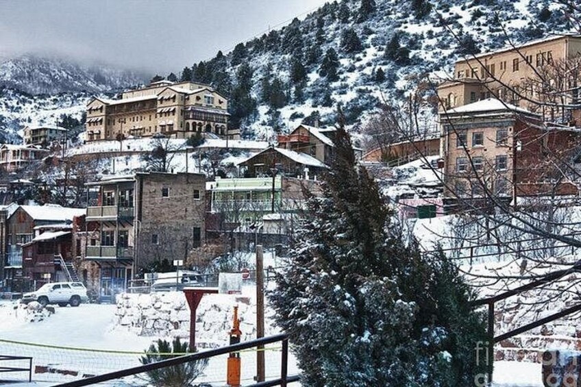 A snow-covered town with buildings, a road, and a mountain in the background. 2