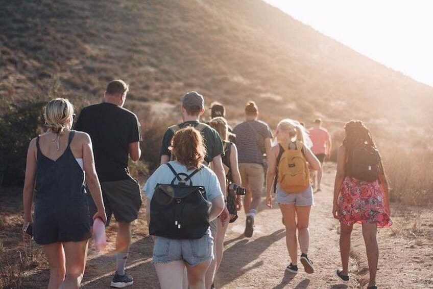 A group of people hiking on a dirt trail with a hilly landscape in the background. 5