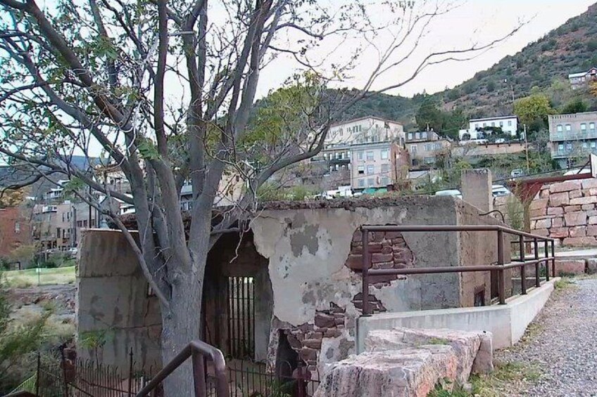 A dilapidated building with a tree in front, a rusty gate, and a staircase leading up to a platform. 4