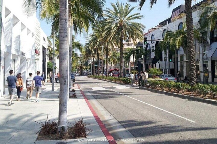 A street lined with palm trees and buildings, with pedestrians walking on the sidewalk. 2