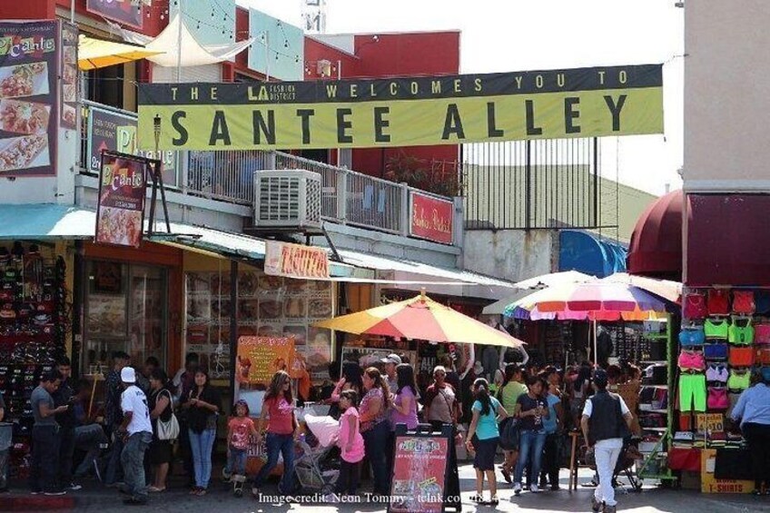 A busy street with a sign reading 'SANTE ALLEY' and various shops and people. 5